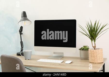 Workplace with computer, plants and lamp on wooden table. Empty black screen Stock Photo