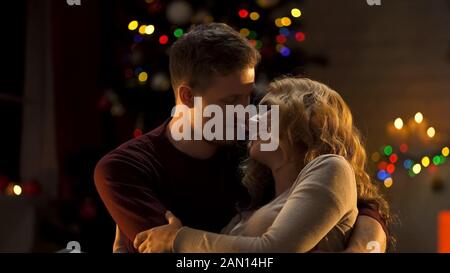 Loving couple embracing tenderly under Christmas tree, first holiday together Stock Photo