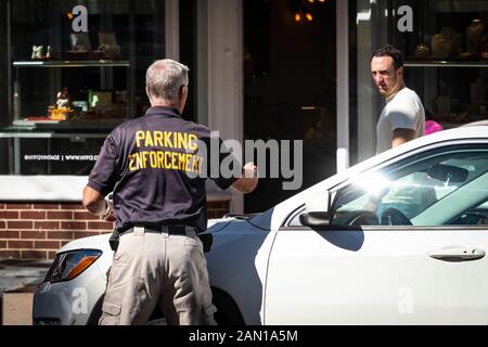 Parking Enforcement man places citation ticket on car - while man gives him disgusted look Stock Photo