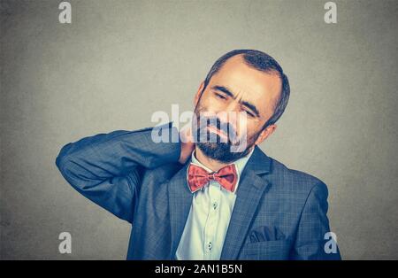 Close up portrait tired middle aged businessman executive with neck pain isolated on gray wall office background. Human face expression emotion, feeli Stock Photo