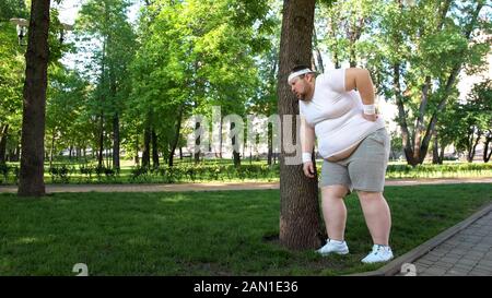 Fat man leaning on tree, tired after workout on fresh air, new healthy habit Stock Photo