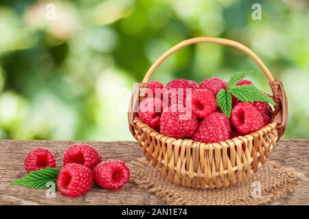 Ripe raspberries with leaf in wicker basket on the old wooden table with blurred garden background Stock Photo