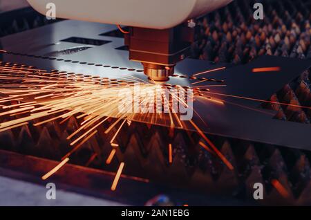 Machine for laser cutting of metal. Laser head cuts the sheet with a beam, sparks scatter in different directions Stock Photo