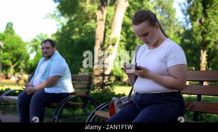 Fat man shy to get acquainted with pretty woman, lady chatting with friend Stock Photo