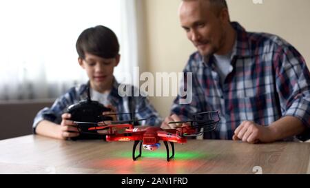 Cheerful boy operating drone with remote control, dad helping son with toy Stock Photo