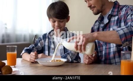 Father pouring milk in plate with corn flakes, son and dad having breakfast Stock Photo