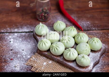 Frozen dough khinkali with spinach. Garnished with Red Chilli, Dill and Parsley. On a wooden background. Copy space. Stock Photo