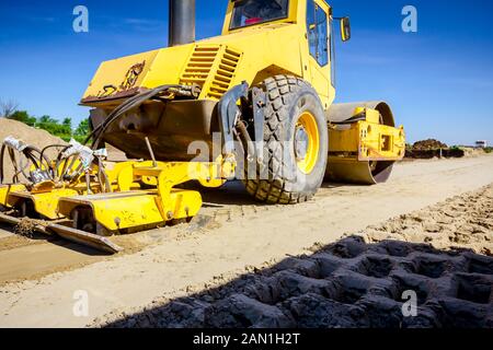 Vibration plate compactor is mounted to the steamroller, compacting sand at road construction site. Stock Photo