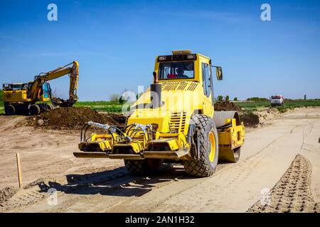 Vibration plate compactor is mounted to the steamroller, compacting sand at road construction site. Stock Photo