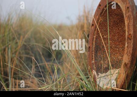 Rusted iron pipe lying on sand beside river for ditching river with blur background. Stock Photo