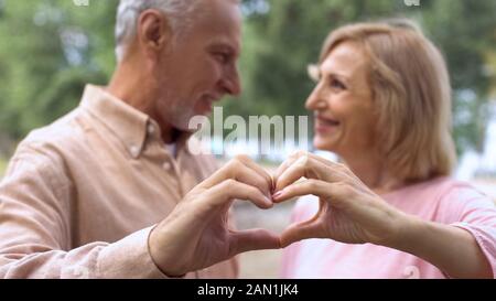 Romantic man and woman making heart sign by hands, looking each other with love Stock Photo