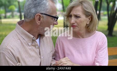 Depressed senior woman looking at husband, holding hands, relations support Stock Photo