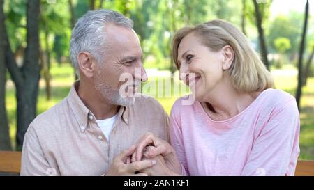 Happy old man and woman looking each other with love and holding hands, date Stock Photo