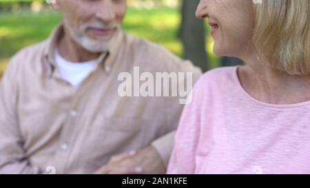 Mature female smiling to handsome man, sitting on bench together, flirting Stock Photo