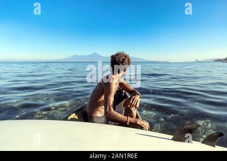 Side view of anonymous man with surfboard sitting in rowboat Stock Photo