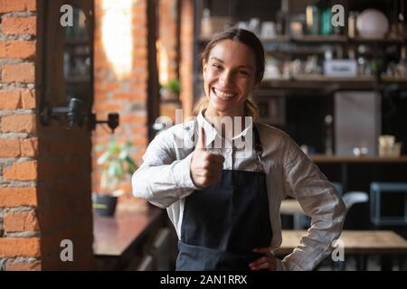 Smiling waitress in apron show thumbs up recommending place Stock Photo