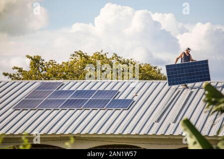 Man carrying solar panel on rooftop. Stock Photo