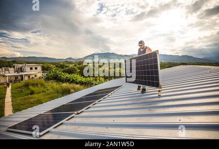 Worker carries solar panel into place on roof during installation. Stock Photo