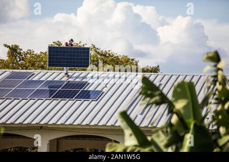 Construction worker carries solar panel on rooftop during install. Stock Photo