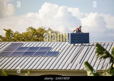 Construction worker carries solar panel across roof during install. Stock Photo