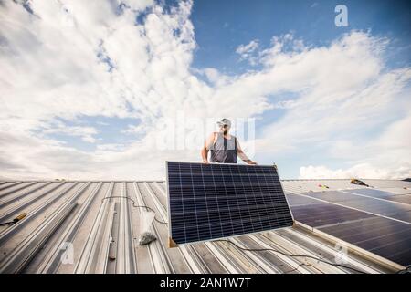 Low angle of construction worker installing solar panels on roof. Stock Photo