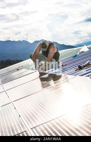 Worker installs solar panels on roof of building. Stock Photo