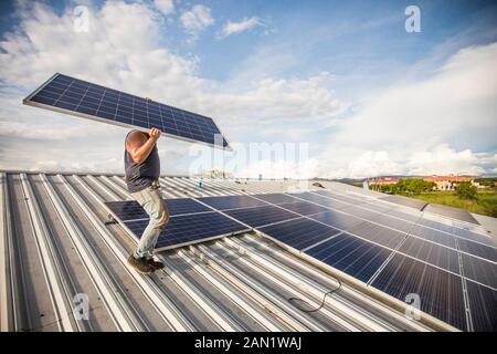 Man carrying solar panel, installing on roof. Stock Photo
