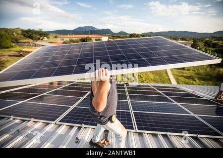 strong construction worker carries solar panel above head on roof. Stock Photo