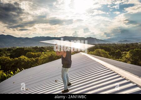 Construction worker carries solar panel above head on roof. Stock Photo