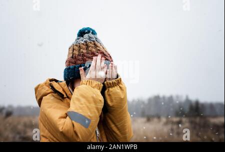 young boy with covering his face with his hands whilst playing in snow Stock Photo