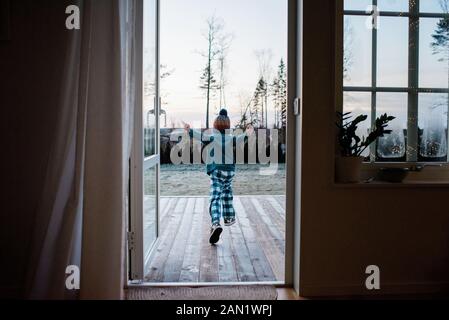young boy running out the backdoor to play outside in winter Stock Photo