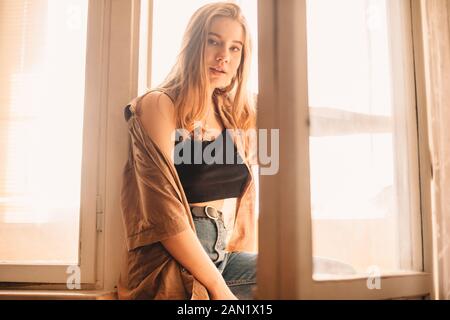 Young woman standing at balcony doorway at home in summer Stock Photo