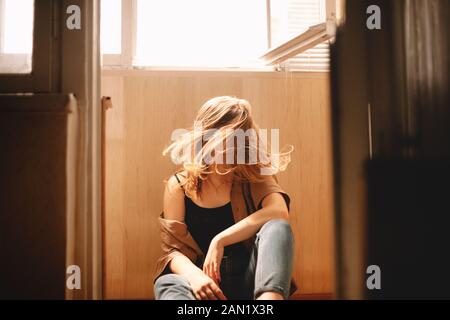 Young woman tossing hair while sitting on floor in balcony in summer Stock Photo