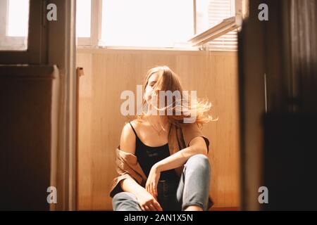 Young woman tossing hair while sitting on floor in balcony at home Stock Photo