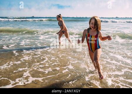 sisters running on beach and splashing in water Stock Photo