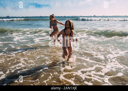 siblings running in water at beach on a sunny day Stock Photo