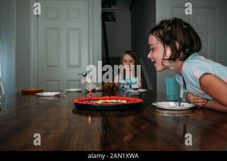 portrait of young girl blowing out birthday candle at a table Stock Photo