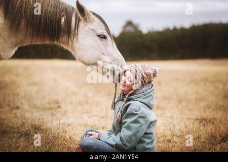 white horse playing with young girls hat while sitting in field Stock Photo