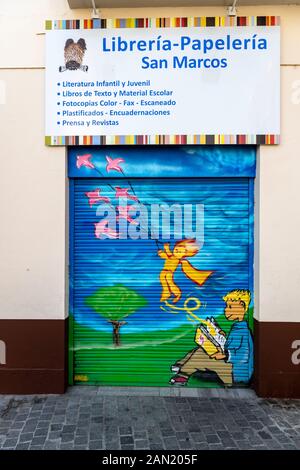 A colourful mural of a child reading a book painted on the shutters of a bookstore / stationers in Plaza de San Marco. Seville Stock Photo