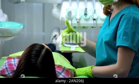 Dentist giving recommendations for teeth care, showing thumb up, approval sign Stock Photo