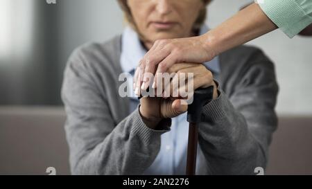 Elderly retired lady sitting on sofa, young woman touching her hands carefully Stock Photo