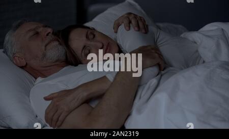 Senior couple lying in bed and hugging lady lying on male chest, strong marriage Stock Photo