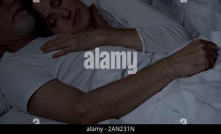 Aged couple peacefully sleeping in bed, wife lying on husband chest, intimacy Stock Photo