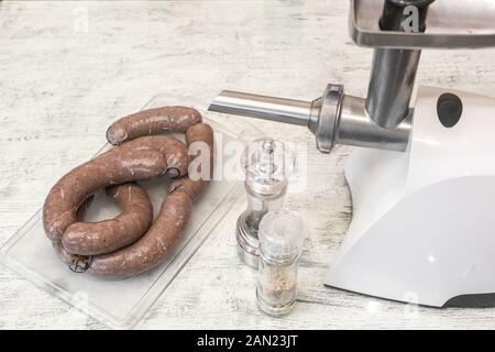 Raw, home-made sausages, pulled tight with thread. Lie on plastic cutting Board. Meat grinder for cooking minced meat and spices for adding piquancy t Stock Photo