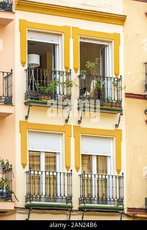 Wrought-iron balconies open out from a colourful apartment building onto Plaza San Juan de la Palma in Seville. Stock Photo