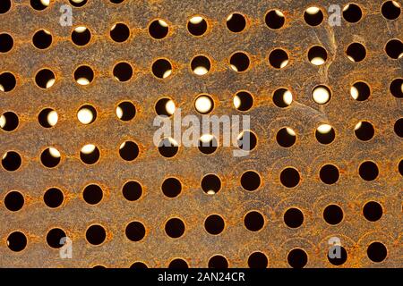 perforated metal with circular holes mostly black, some with translucent white light Stock Photo