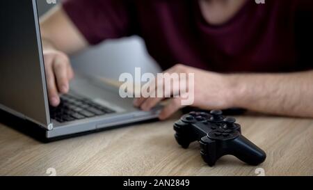 Male playing video games, joystick lying on table near laptop, gaming addiction Stock Photo
