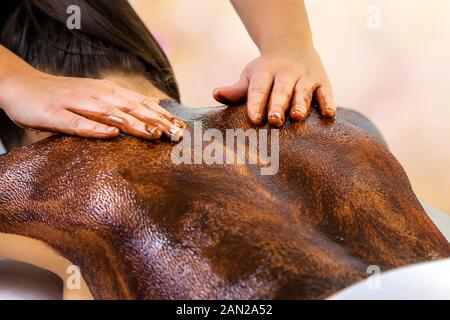 Close up detail of hands doing back massage on woman. Therapist using hot antioxidant chocolate wax on body. Stock Photo