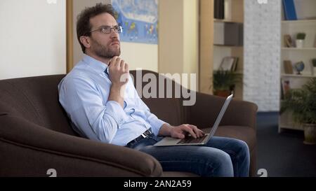 IT freelance specialist working laptop on sofa, thinking about new project Stock Photo