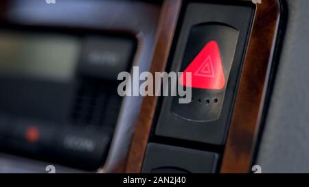 Pressed and glowing emergency car hazard warning flasher button on dashboard Stock Photo